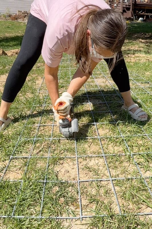 Cutting a galvanized wire panel with an angle grinder while wearing work gloves to build an arched garden trellis