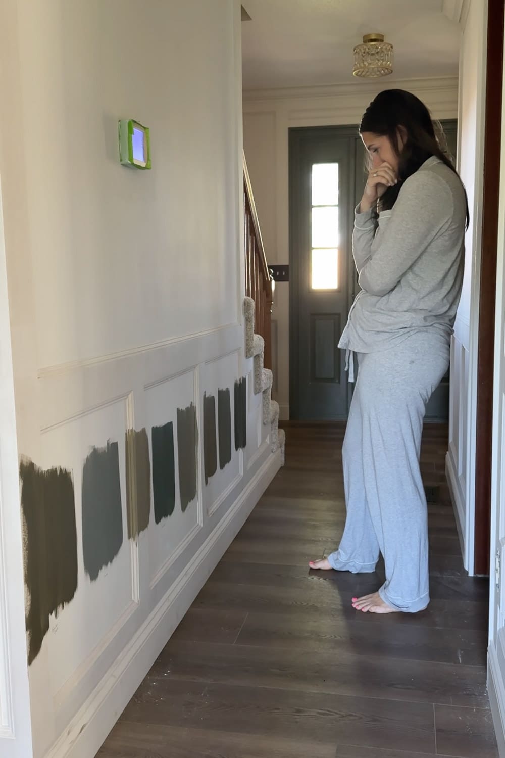 Testing moody green and dusty blue paint swatches on primed picture frame moulding while decorating a narrow hallway