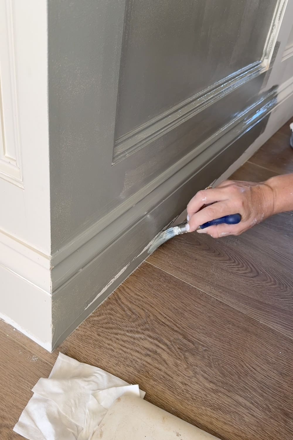 Cutting in Sherwin-Williams Taiga along the baseboard with an angled brush while decorating a narrow hallway