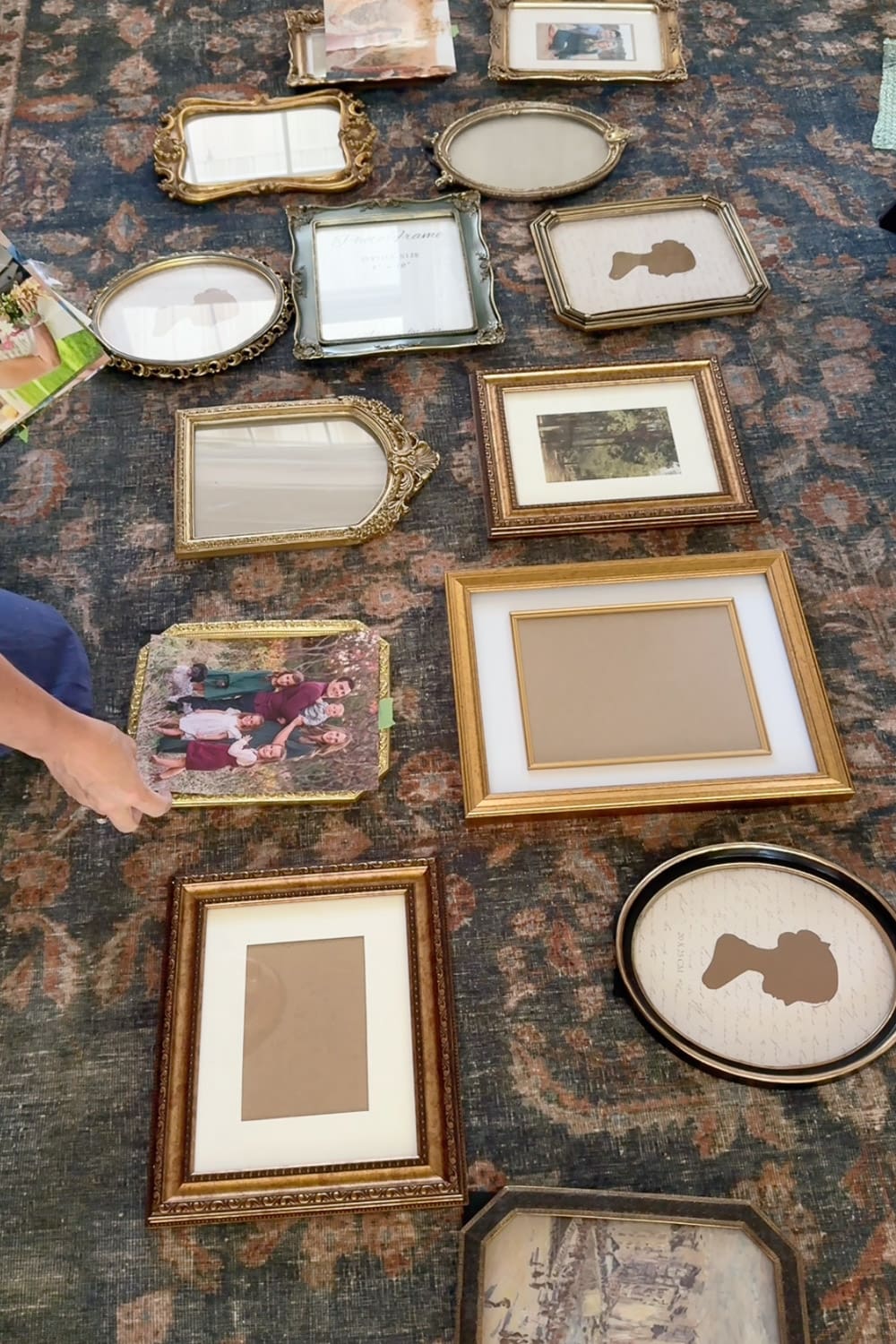 Planning a hallway gallery wall by arranging mismatched gold frames on a patterned rug before hanging