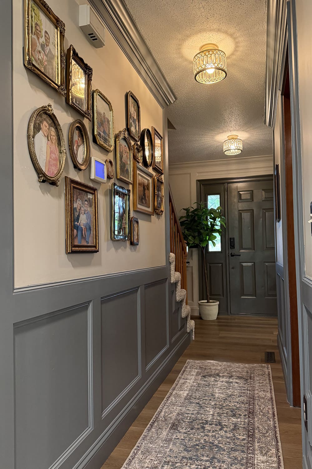 Decorating a narrow hallway with a mismatched frame gallery wall, gray wainscoting, and a patterned runner leading to a dark front door