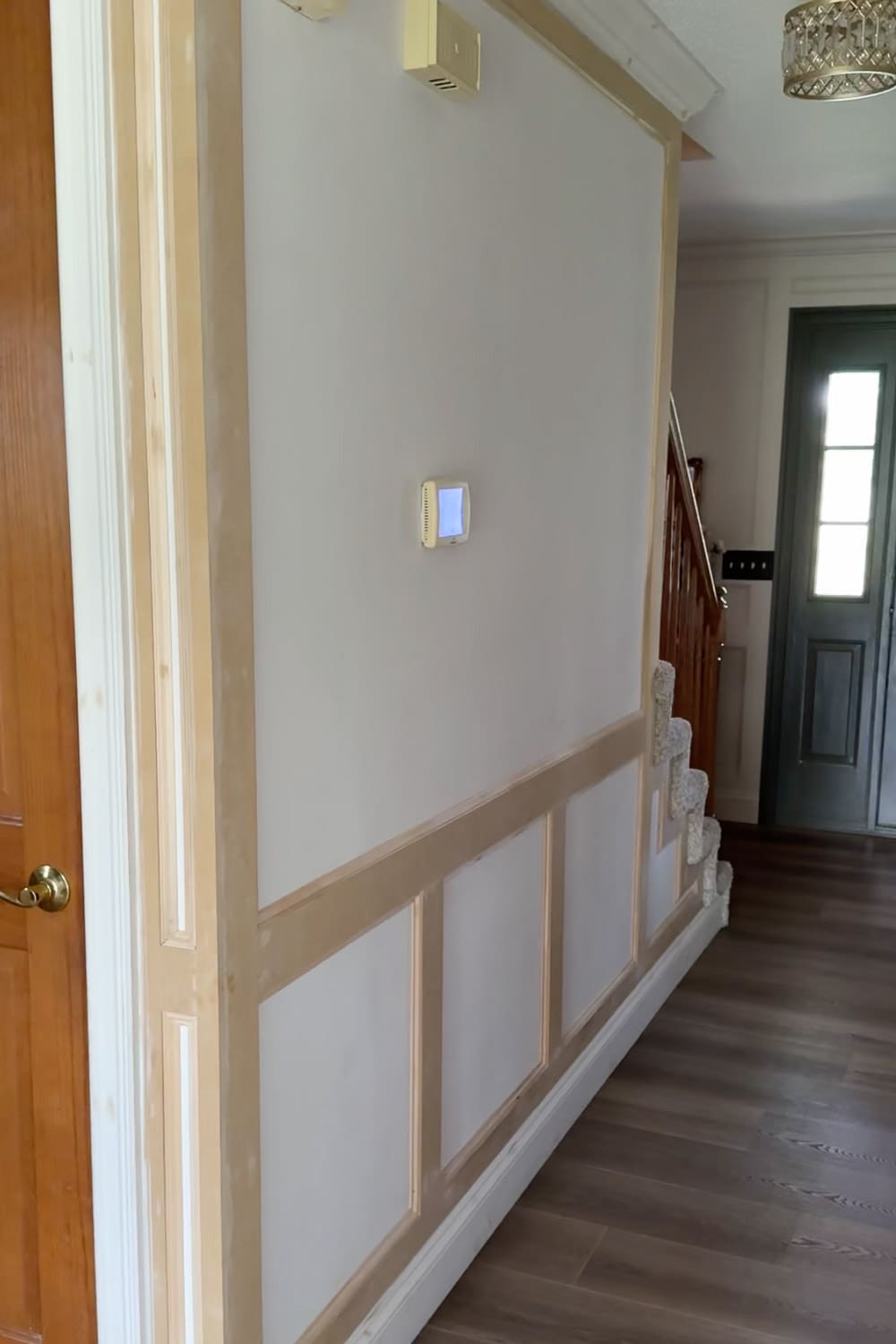 Freshly installed picture frame moulding on the hallway wall before filling, caulking, and painting, showing raw wood trim