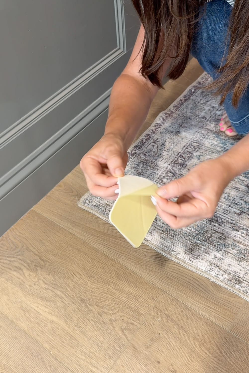 Peeling the backing off a non-slip rug pad to keep the hallway runner from sliding in a high-traffic area