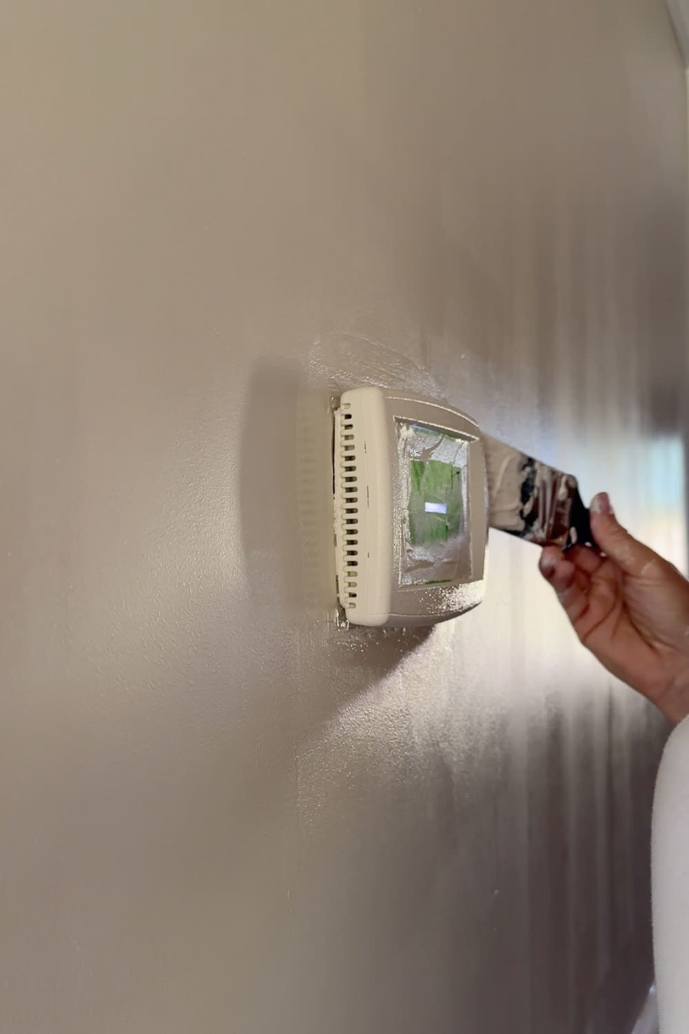 Brushing Sherwin-Williams Accessible Beige over the primed thermostat to disappear it into the wall while decorating a narrow hallway