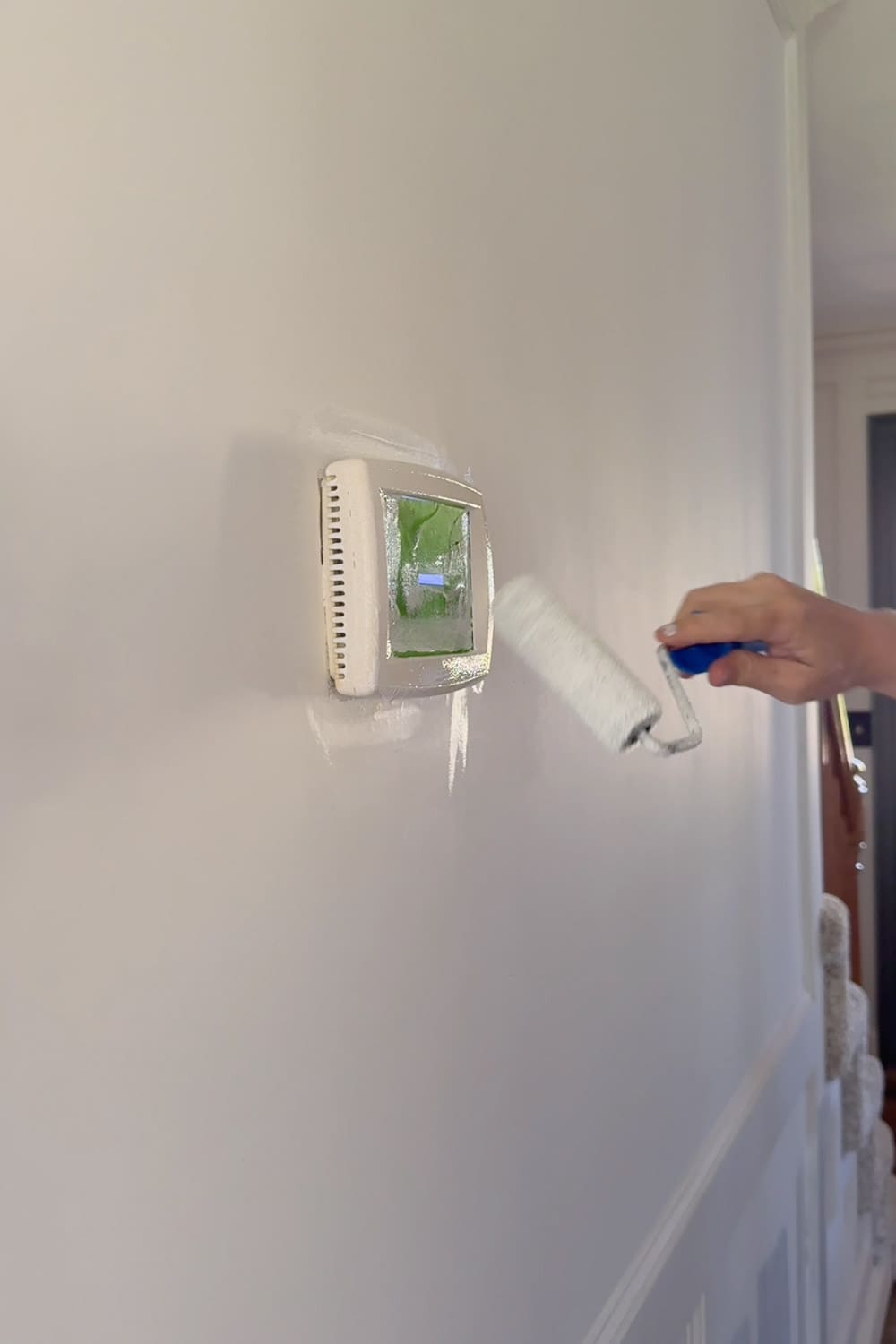 Rolling primer over a taped-off thermostat as the first step to blending it into the hallway wall