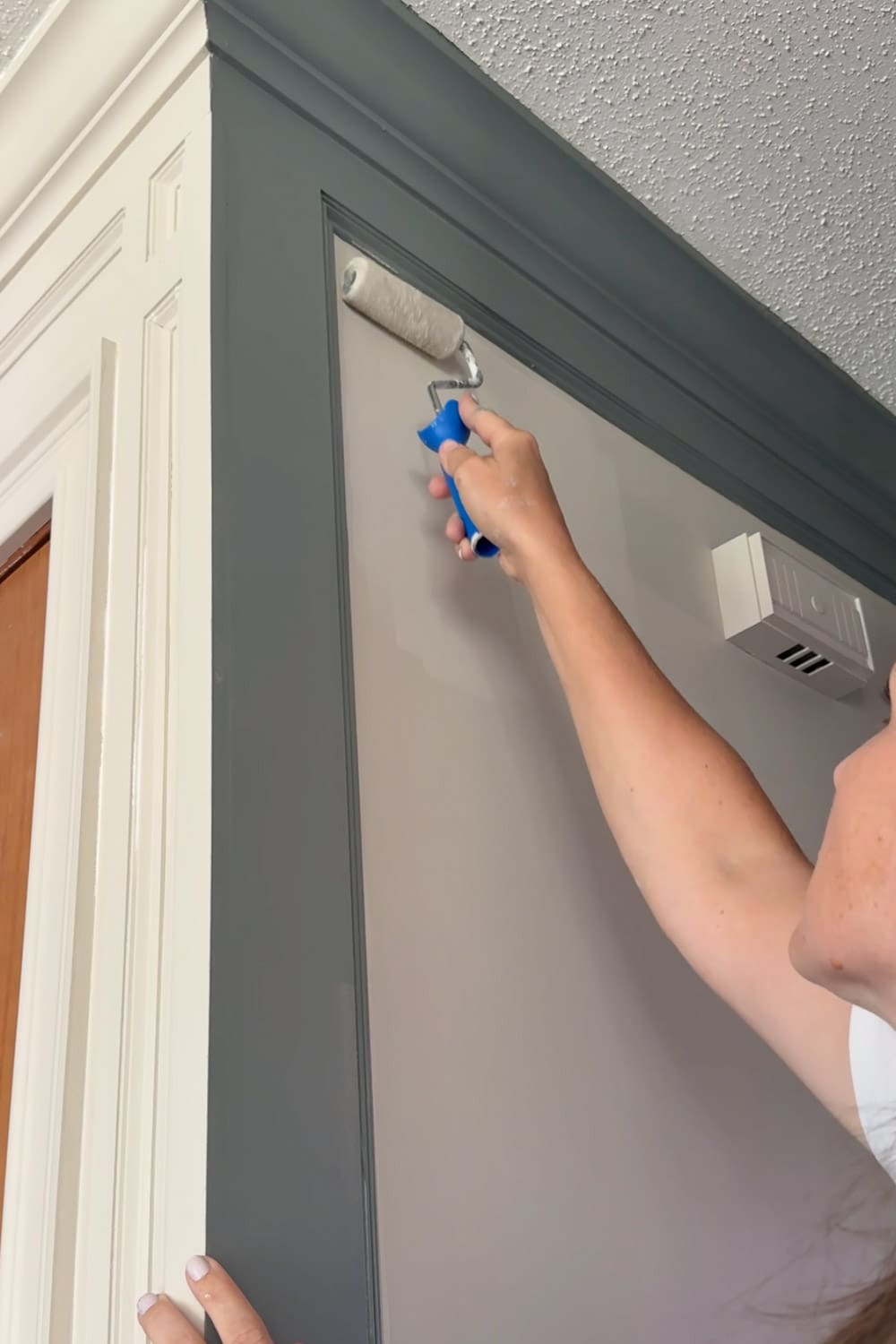 Rolling Sherwin-Williams Accessible Beige onto the wall next to the dark Taiga picture frame moulding in a narrow hallway