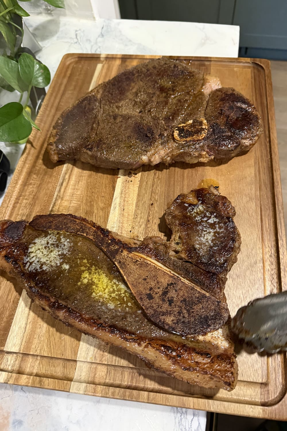 Two seared slices of beef roast resting on a wood cutting board with melted butter on top