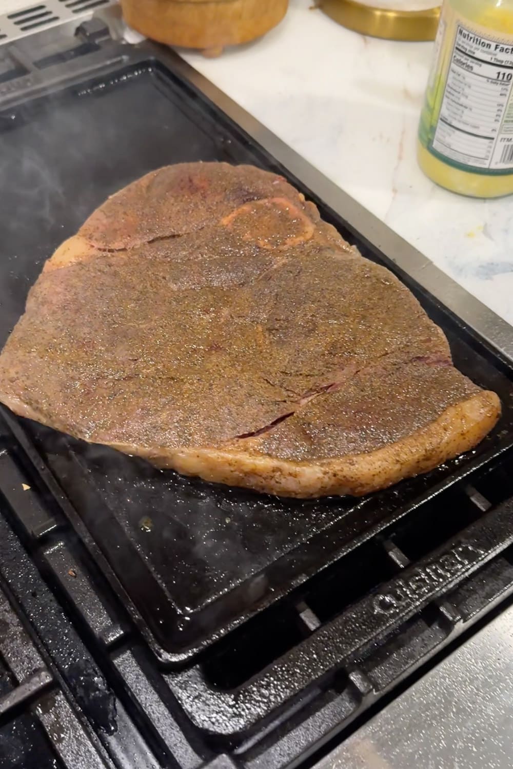Seasoned beef searing on a hot cast iron griddle on the stove