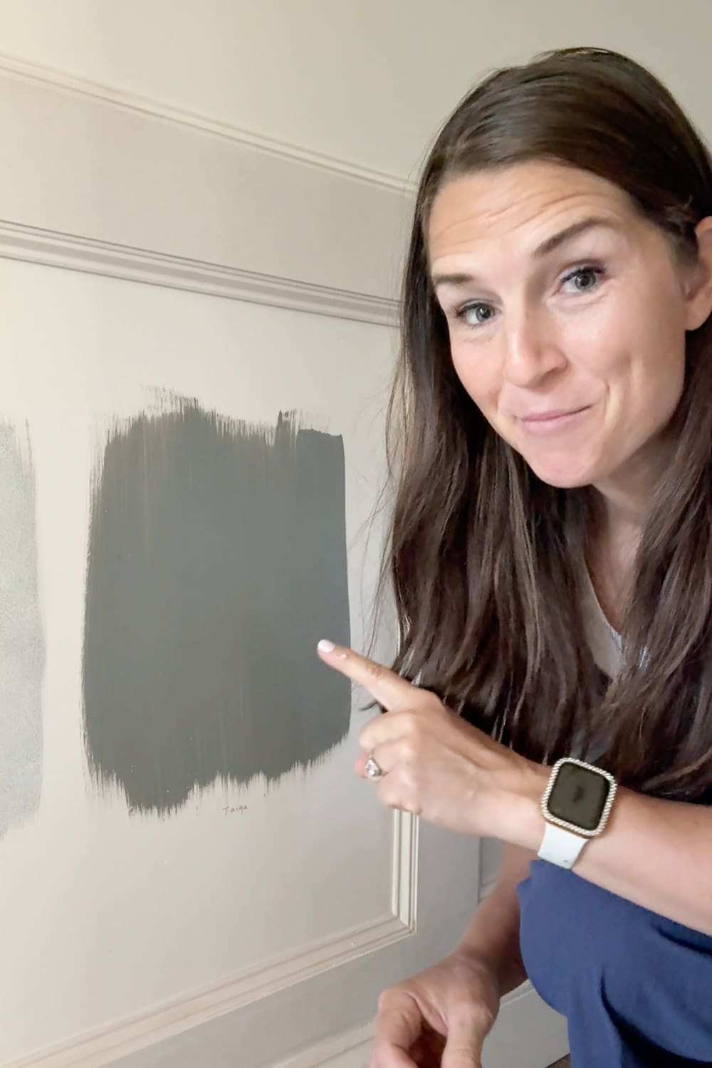 Crystel pointing to the winning paint color, Sherwin Williams Taiga, a moody green-gray swatch on the primed hallway moulding