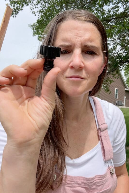 Crystel holding up a black end cap fitting used to seal a soaker hose in a raised garden bed setup