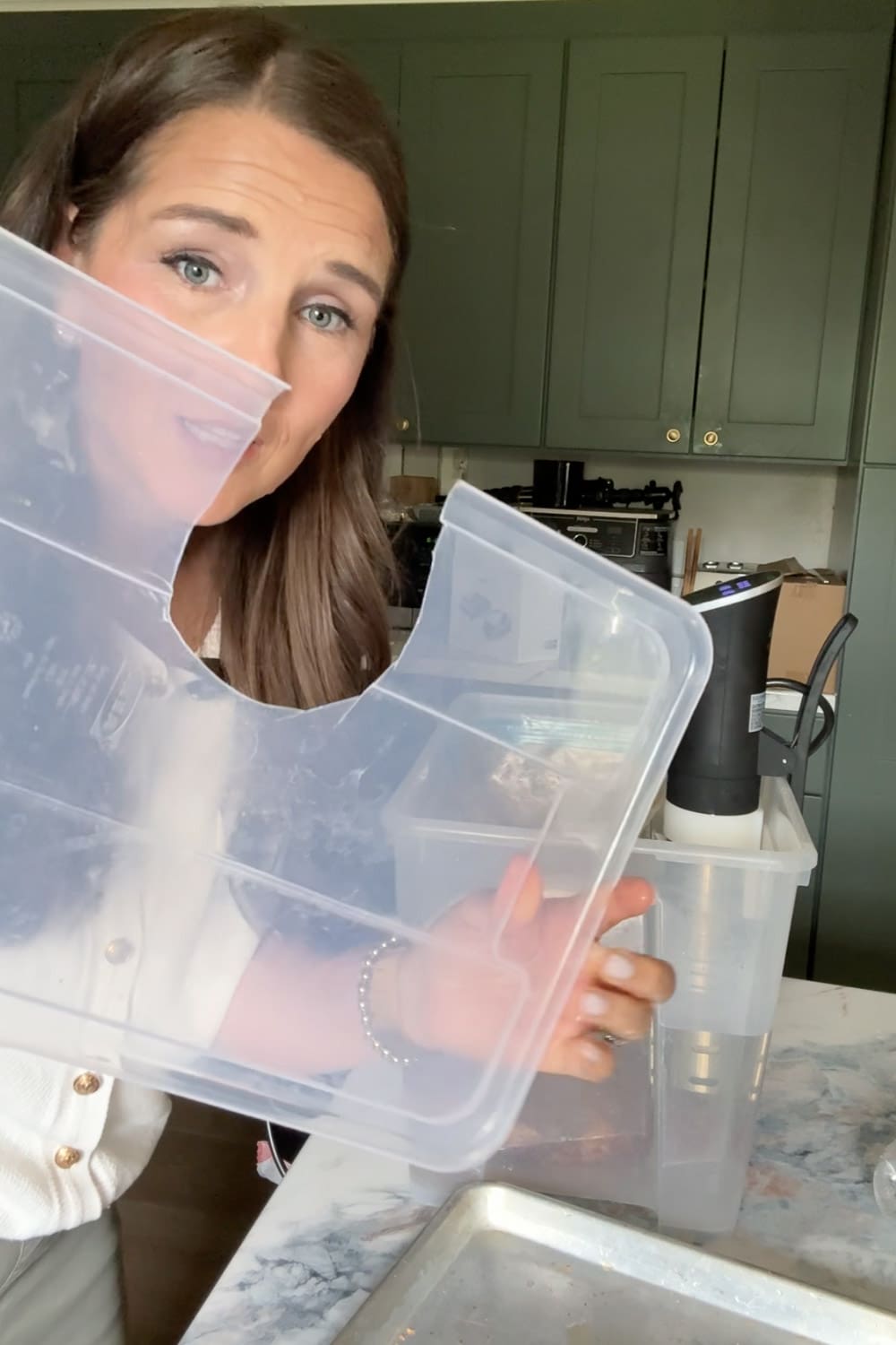 Holding a clear plastic container used as a sous vide water bath with the immersion circulator behind
