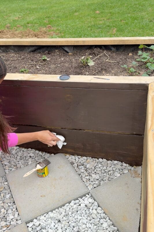 Applying Cabot Cordovan Brown stain to a raised garden bed with a rag for an even finish