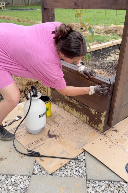 Spraying stain and wiping it into a raised garden bed with a sponge for even coverage