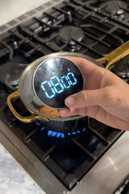 Crystel holding a digital timer set to 8 minutes over the pot of boiling water, timing the batch while hard boiling.