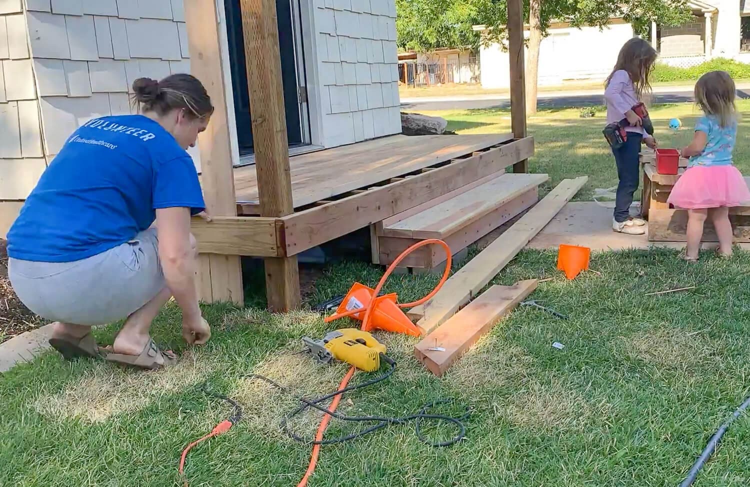 Crystel attaching wood skirting to the base of the DIY front porch while her two daughters play nearby.