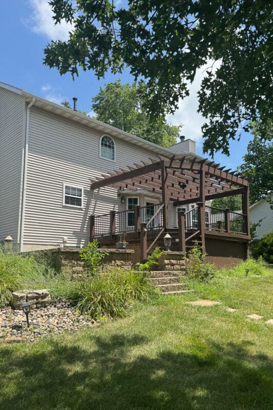 Raised wood deck with a stained pergola and black metal railing in the backyard before it was torn out