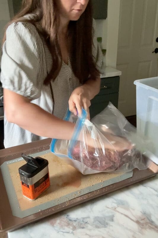 Crystel placing a seasoned chuck roast into a bag next to a tin of Traeger rub, prepping the sous vide chuck roast