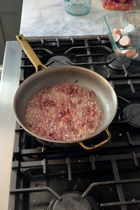 Chopped beet stems simmering and softening in garlic butter, turning the liquid a pretty pink as they cook