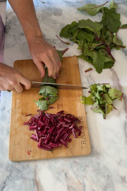 Close up of how to cook beet greens by slicing the colorful stems into bite sized pieces on a Traeger board