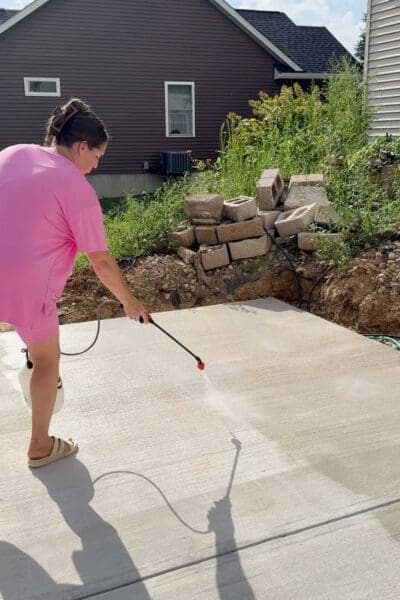 Crystel using a pump sprayer for concrete patio sealing, with the spray fan visible on the new concrete patio.
