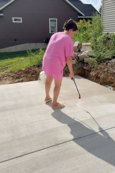 Crystel using a pump sprayer for concrete patio sealing, with the spray fan visible on the concrete