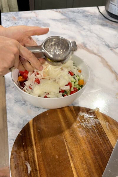 Crystel squeezing fresh lemon over the cucumber, tomato, and white onion salad for Greek lemon chicken rice bowls