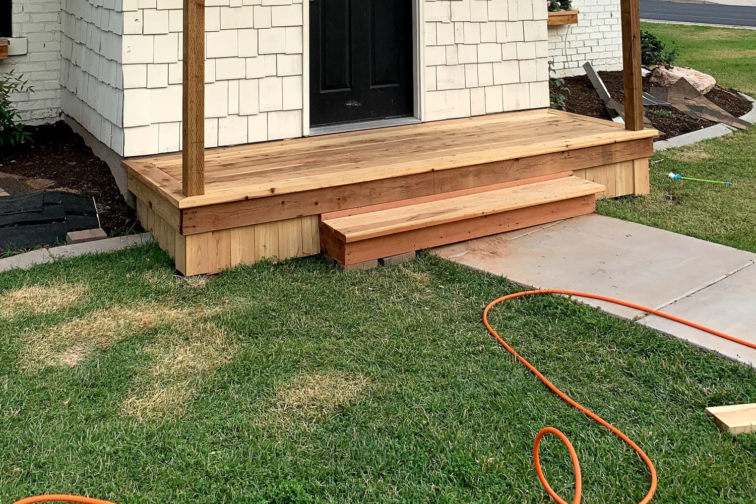 Completed DIY porch box step wrapped in cedar, leading down to the concrete walkway from the front door.