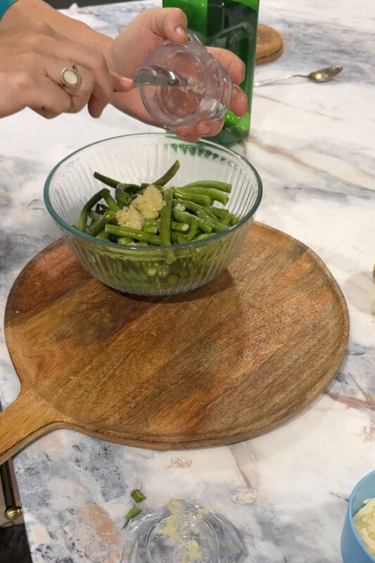 Crystel adding freshly minced garlic to a bowl of trimmed green beans.