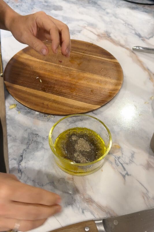 Crystel adding salt and pepper to the lemon, olive oil, and oregano marinade.