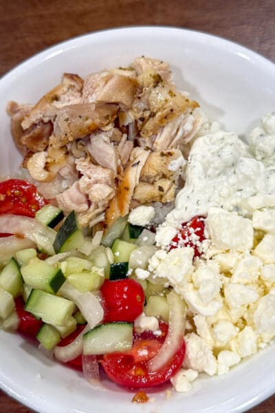 Overhead view of Greek lemon chicken rice bowls with sliced chicken, cucumber-tomato salad, white onion, feta, and tzatziki over rice