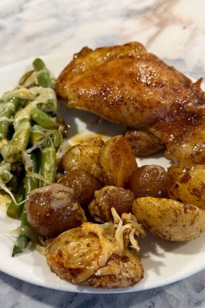 Close-up of a glazed chicken thigh with crispy roasted potatoes and parmesan green beans, part of this sheet pan chicken thighs dinner.