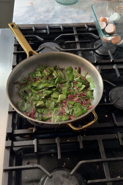 Chopped beet green leaves added to the pan of cooked stems and garlic butter, just starting to wilt down