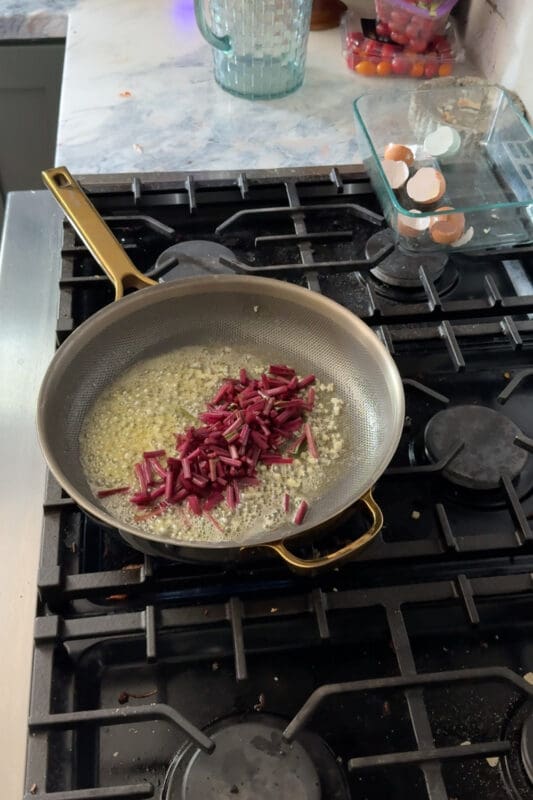 Crystel adding chopped ruby beet stems to a pan of sizzling garlic butter to start cooking the tougher stems first