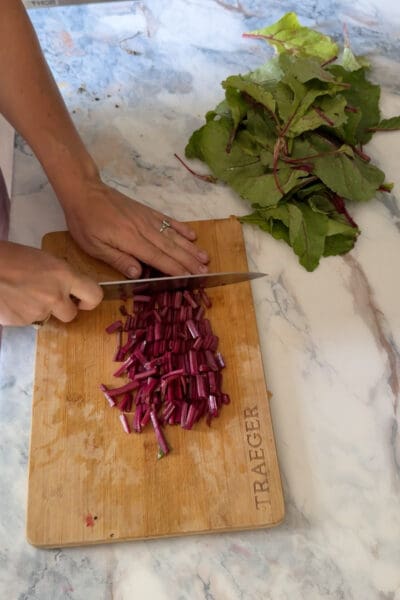 Crystel chopping beet stems into small pieces on a wooden cutting board with separated leaves and stems nearby