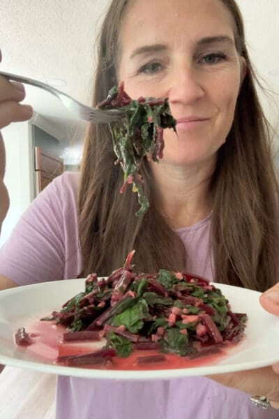 Crystel smiling and holding up a forkful of cooked beet greens over a plated serving to show how tender and tasty they turned out