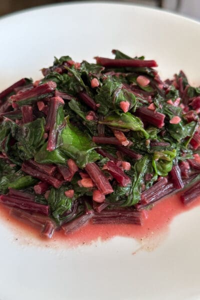 Close up of how to cook beet greens with sauteed garlic and magenta stems glistening on a white plate
