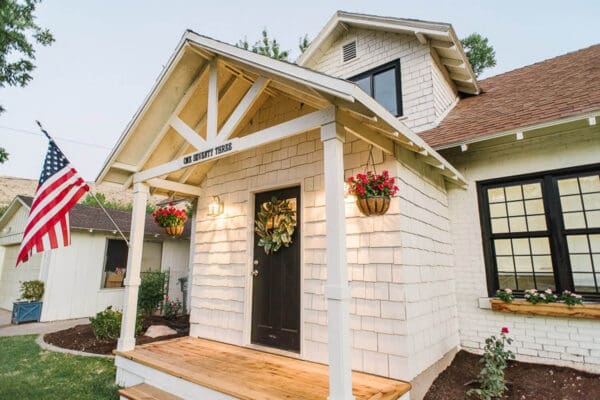 White craftsman gable porch roof with American flag and hanging baskets at dusk