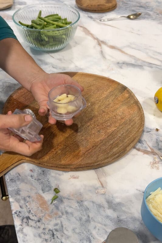 Crystel adding peeled garlic cloves to a handheld garlic twister to quickly mince them for the green beans.