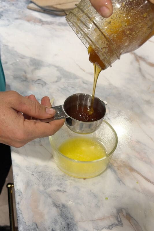 Crystel pouring honey from a measuring cup into a bowl of melted butter to make the glaze.