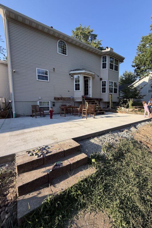 Freshly poured concrete patio where an old wood deck used to be, with patio furniture and bare ground still to be landscaped