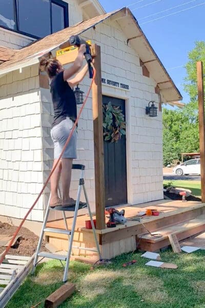 Woman on ladder checking post for vertical plumb while holding level