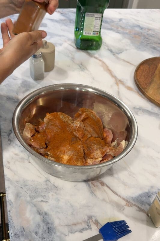 Crystel seasoning boneless chicken thighs with smoked paprika in a metal mixing bowl.