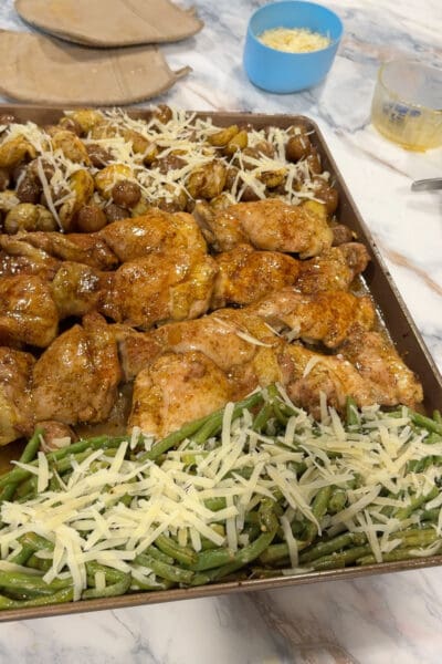 Finished sheet pan chicken thighs with glazed potatoes and green beans, all topped with shredded parmesan.
