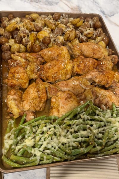 Honey glazed sheet pan chicken thighs fresh from the oven with parmesan potatoes and cheesy green beans on one pan.