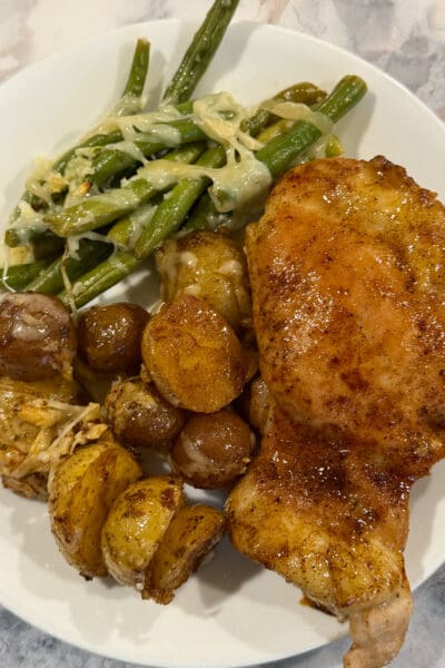 Overhead plate of sheet pan chicken thighs with crispy roasted potatoes and garlicky parmesan green beans on a marble counter.