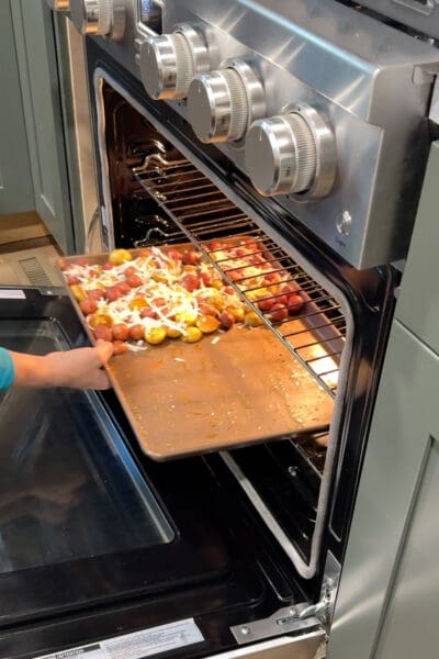 Crystel sliding a sheet pan of parmesan-topped baby potatoes into the oven, the first step for sheet pan chicken thighs.