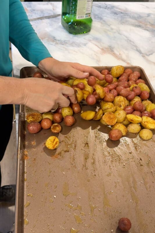 Crystel tossing halved baby potatoes with olive oil and smoked paprika on the pan for these sheet pan chicken thighs.