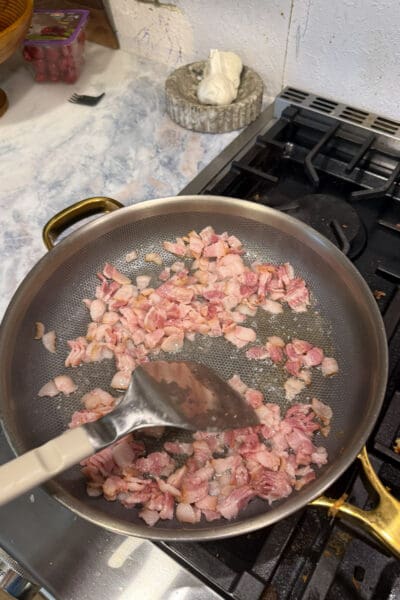 Chopped bacon crisping in a skillet on the stove, the first cooking step for shrimp and corn succotash