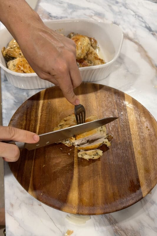 Crystel slicing the rested lemon-oregano chicken on a wooden board for Greek lemon chicken rice bowls