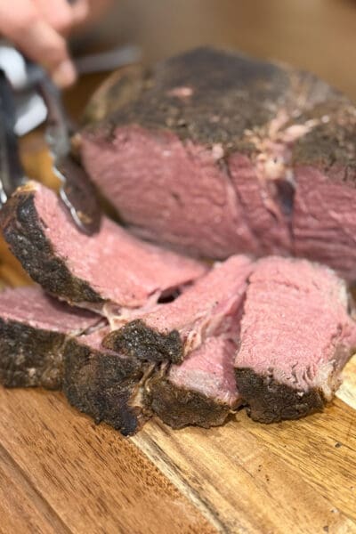 Close-up of sliced sous vide chuck roast on a wood cutting board with an even pink center and a well-seasoned seared crust